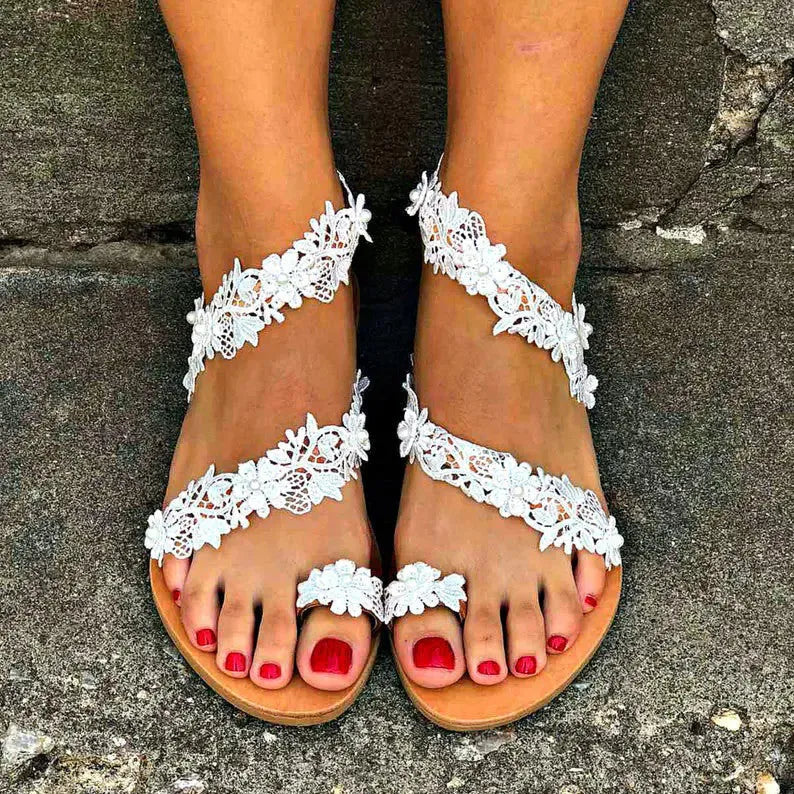 White women's slip-on flat shoes with floral and rhinestone decoration on the upper.