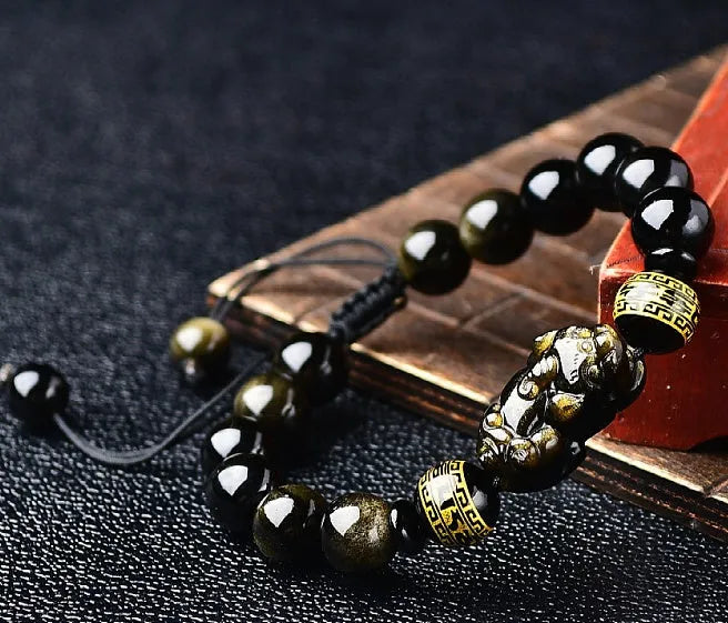 Golden obsidian bead Pi Xiu bracelet with hand-woven design on a wrist.