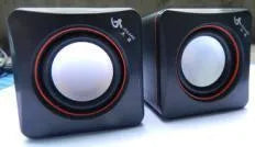 Black small square USB-powered computer speaker on desktop next to monitor