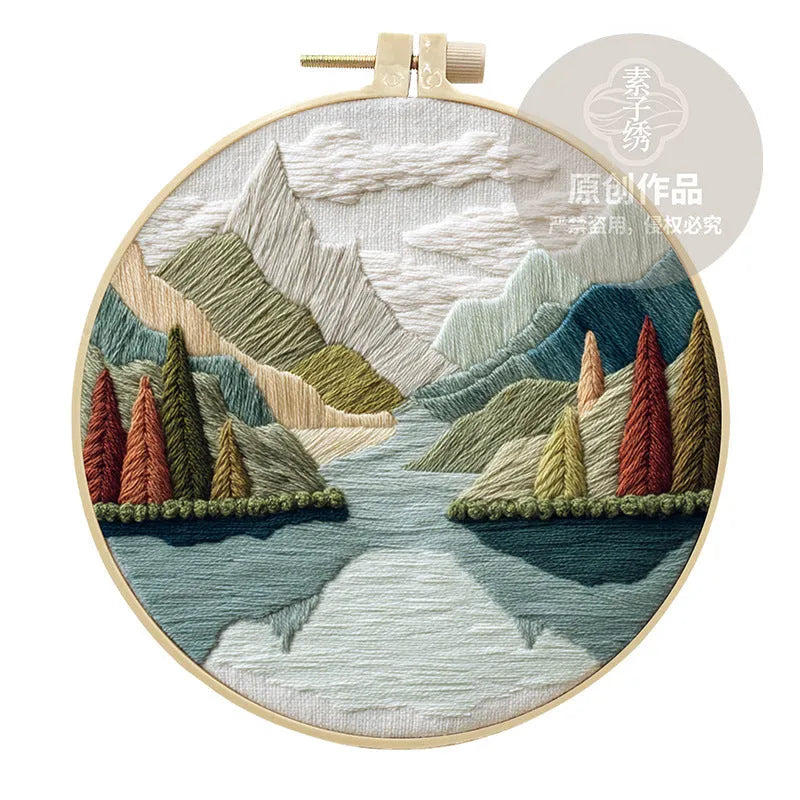 DIY embroidery kit components: printed cotton landscape fabric, embroidery threads, needles, and a bamboo hoop.