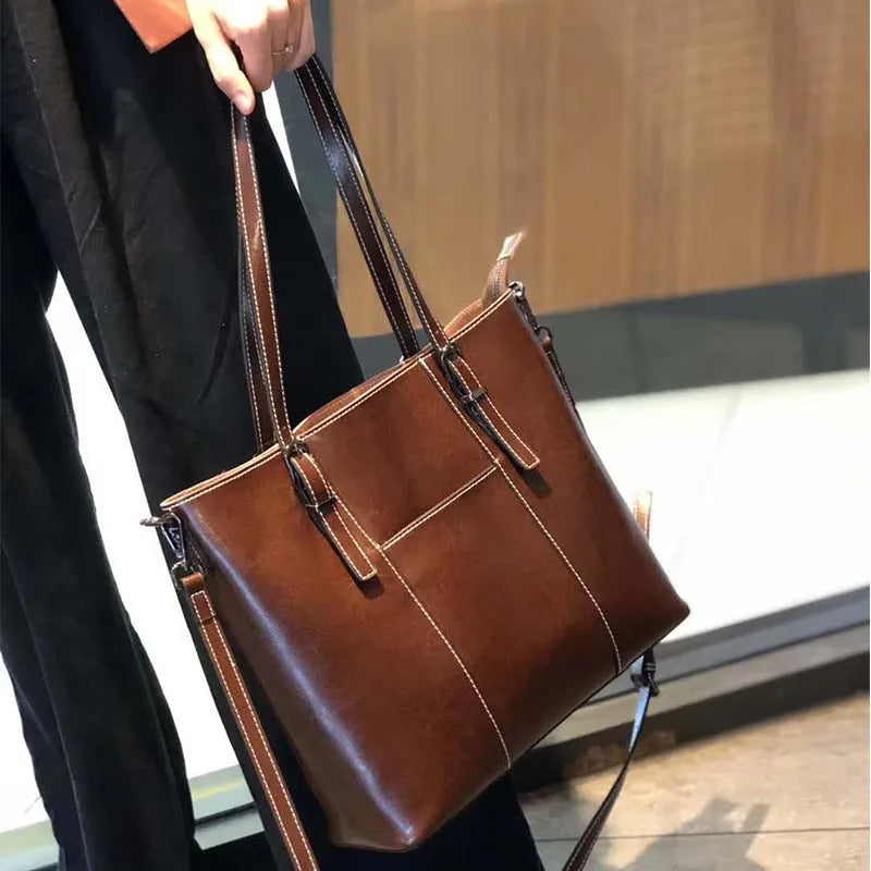 Brown genuine leather retro women's shoulder tote bag with three straps on a table.