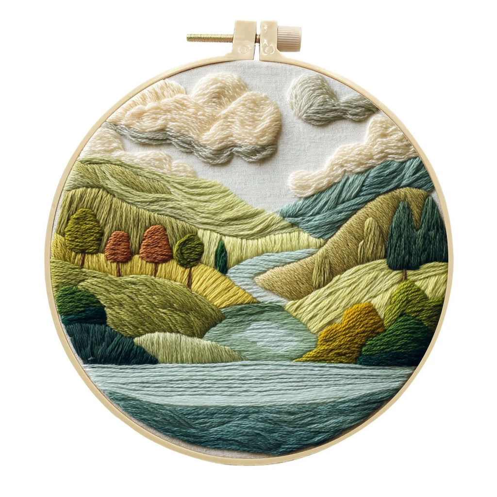 DIY embroidery kit components: printed cotton landscape fabric, embroidery threads, needles, and a bamboo hoop.