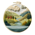 DIY embroidery kit components: printed cotton landscape fabric, embroidery threads, needles, and a bamboo hoop.