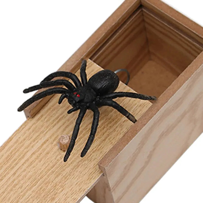 Wooden prank box with lid open showing a lifelike jumping spider inside on a white background.