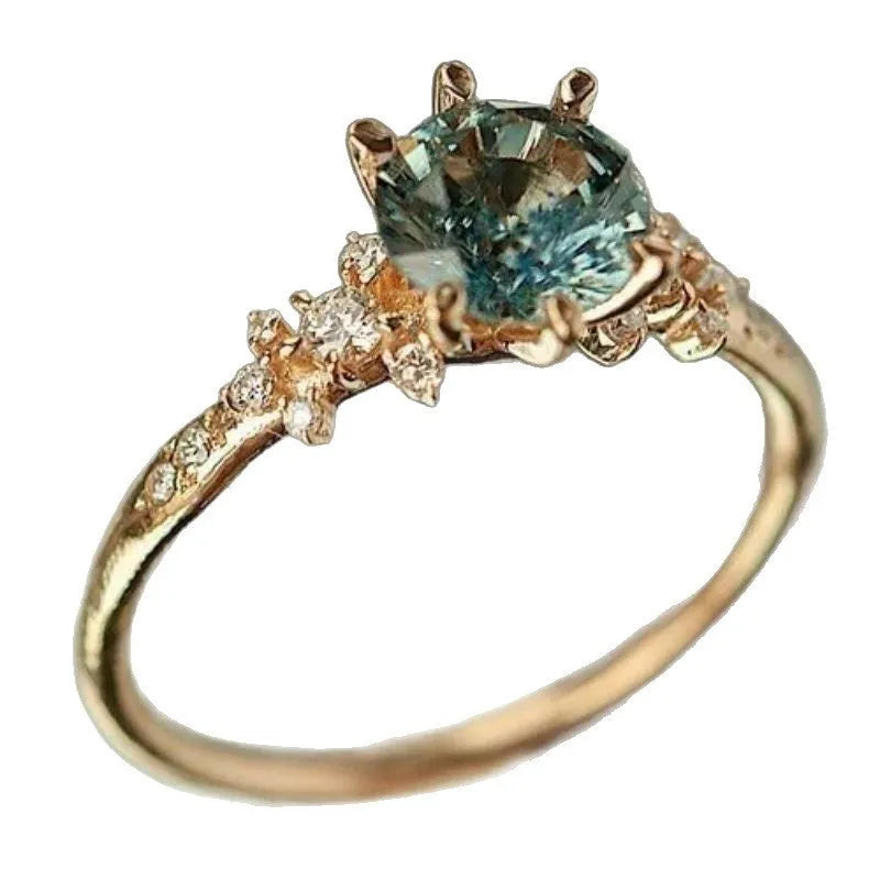 Gold geometric ring with a claw-set zircon stone and a textured square pattern band.