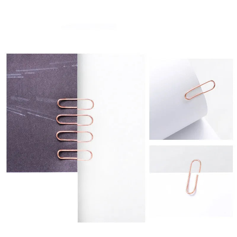 Box of 100 small rose gold heart-shaped metal paper clips on a white surface.