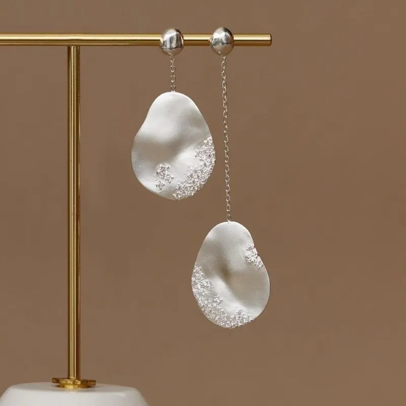 A pair of asymmetric gold-plated flower earrings with zircon detail, shown in silver and gold colour options.