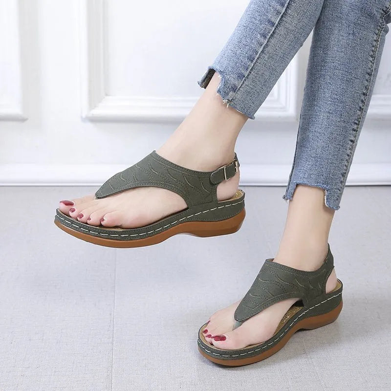 Women's beige wedge heel flip flop sandals with an adjustable buckle strap on a wooden deck.