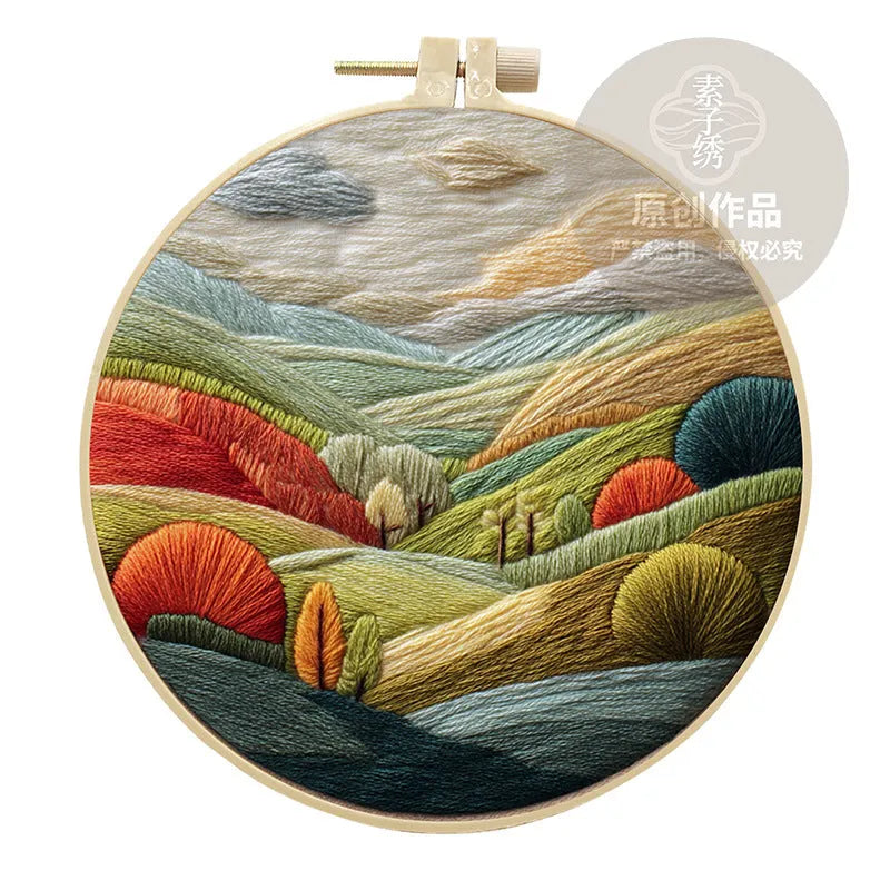 DIY embroidery kit components: printed cotton landscape fabric, embroidery threads, needles, and a bamboo hoop.