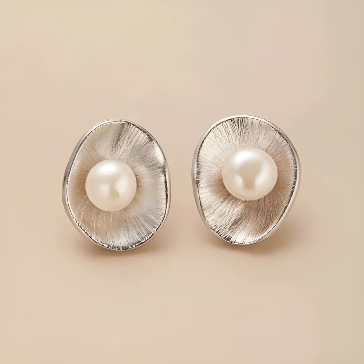 Gold tone geometric stud earrings with a central freshwater pearl on a silver needle post.